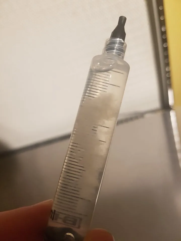 Filled spore syringe held up to the light, showing a cloud of suspended spores in the barrel